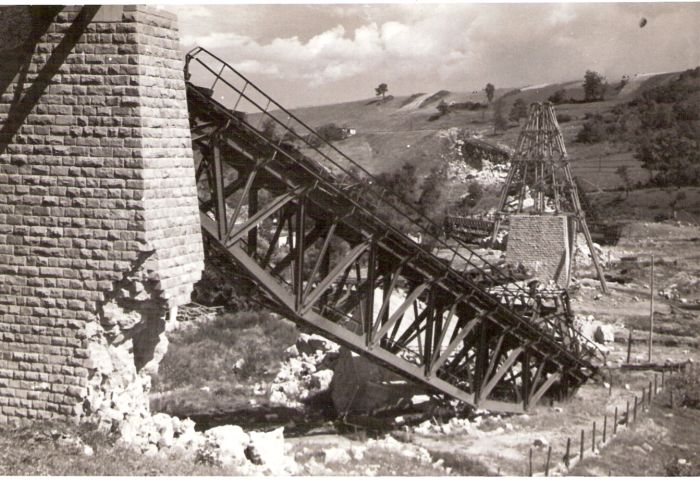  Hanušovce - trosky žel. mosta v pahork. krajine - lichobežn. most. polia v na zemi, rozváľané kamen. piliere, jeden v stavbe s lešením. Vľ. rozstrel. pilier. Text: Hanušovce - zničený most. Foto: ČSD, cca 1945. 171 x 115 