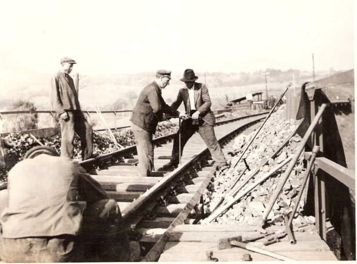  Pokl. zvršku na trati v prech. na most. Zatáčanie vrtúl. O zábradlie oprené náradie. Ľudia v žel. Rovnoš. i civile. Vzadu hory. Text: Žel. zamestn na oprave trate Handlová - Horná Štubňa. Anon., cca 1945. 173 x 122 