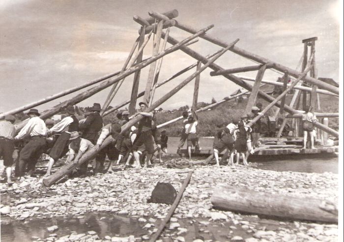  Ľudia v civile pri vztyčovaní drev. piliera (pre lanovku ?) v riečke. Vzadu pahorok s dedinsk. domami. Text: Povojnová obnova zničeného Slovenska, stavanie pilierov. Foto: ČSD, Kľučka, cca 1945. 168 x 122 