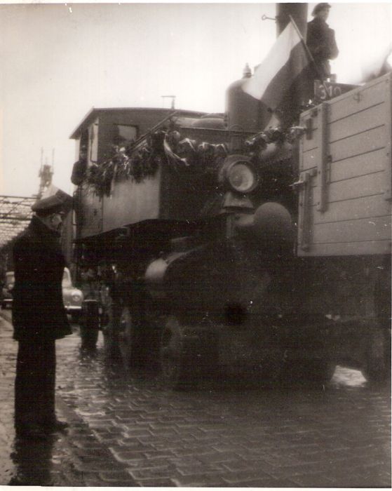  Preprava ozdob. rušňa 310.4/5 (?) na podv. Cullmayer za Tatrou T 111 na petržalskej strane bratisl. mosta. Dlažba, ľudia v žel. rovnošate i prac. Text: Povojn. obnova prevádzky v okolí Petržalky. Anon., cca 1945. 110 x 135 