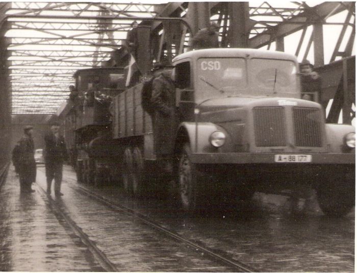  Preprava ozdob. rušňa 310.4/5 (?) na podv. Cullmayer za Tatrou T 111 na bratisl. moste. Dlažba s koľajami električky, ľudia. Text: Povojn. obnova prevádzky v okolí Petržalky. Anon., cca 1945. 140 x 105 