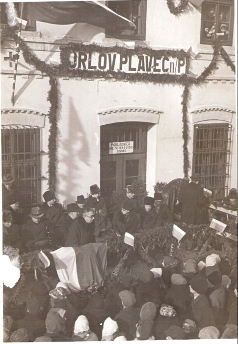  Orlov - skup. činovníkov na ozdob. tribúne pred výpr. bud. s pôv. fasád. výzdobou a nápisom ORLOV PLAVEČ n/P. Sledujúci ľudia. Text: Znovuotv. trate Orlov - Plaveč po 2. svet. vojne. Anon., cca 1945. 118 x 169 