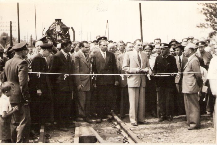  Rečník pri strihaní pásky. Za ním zástup ľudí, vzadu ozdobené čelo 387.0. Telegraf. tyče. Text: Sprevádzkovanie mosta cez Váh pri Šali po 2. svetovej vojne. Anon., cca 1950. 170 x 110 