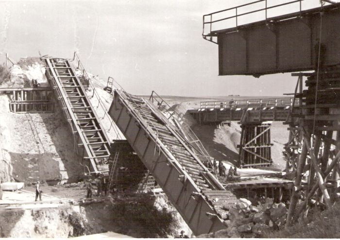  Trosky mosta s plechovými nosníkmi - vľavo šikmo oprené dve most. polia, vpravo jedno uložené na proviz. pilieri.Vzadu provizórny most. Text: Zničené železničné mosty pri Prešove. Anon., cca 1945. 170 x 120 