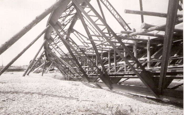  Trať Leopoldov - Hlohovec. Trosky poloparabolic. mosta cez Váh. Pohľad zboku pozdĺž mosta na šikmo na brehu uložené pole s vloženou lávkou pre peších. Text: Most v Hlohovci. Foto: Morávka, cca 1945. 175 x 115 