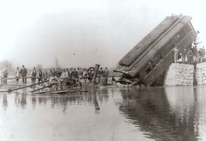  Nehoda - vo vodnej ploche ponorený rušeň radu 310.4, o jeho kabínu sa opiera šikmo sklonený dvojnápr. os. vozeň 2. tr. MÁV, ktorý druhým koncom visí na kamennom pilieri. Anon., cca 1900. 178 x 129, Repro : T. Grófová 