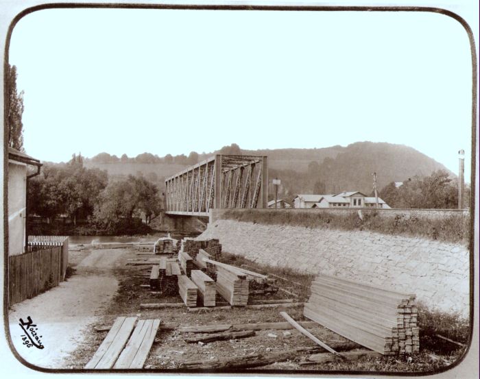  Priamopásový priehrad. most nad riekou, vpredu sklad dosiek a roh budovy, vpravu za riekou priemyseľné budovy. Text: Most nad Hronom pred Banskou Bystricou. Foto: Kóczány, 1896. 222 x 175 