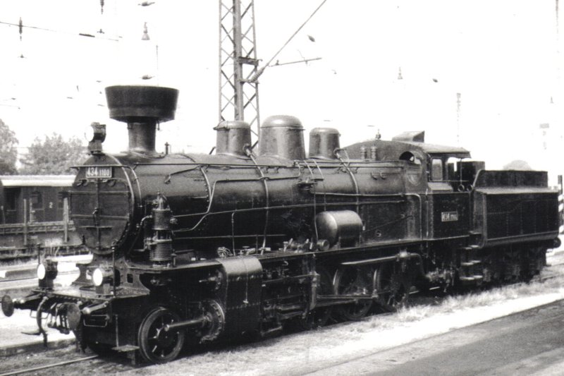  Parný rušeň 434.1100 v žst. Nymburk. Pohľad zľava zpredu. Vzadu časť Ce a Nas, troleje, osvetľ. stožiare. Anon., 17.9.1982. 122 x 84 