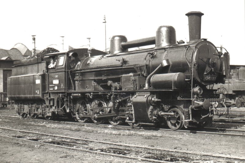  Parný rušeň 434.2191 pravdepodobne v depe Nymburk. Pohľad zprava zpredu. Vpravo vzadu časť 403.303. Vzadu hala depa, osvetľ. stožiar. Foto: P. Vančura, cca 1965. 145 x 103 