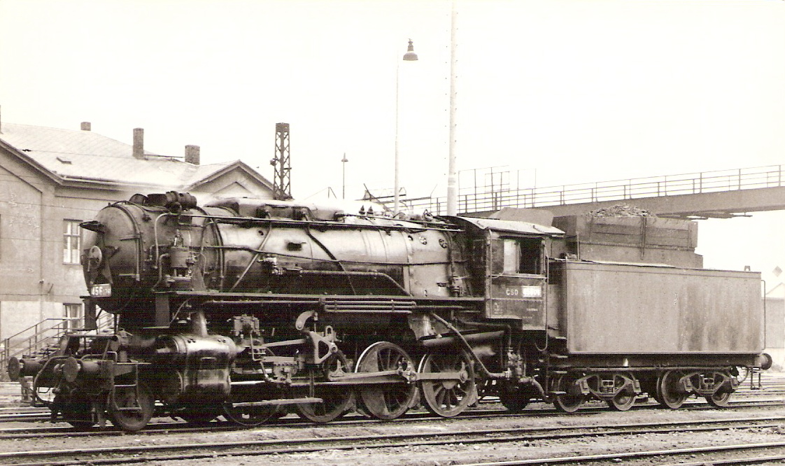  Parný rušeň 456.176. Pohľad zľava zpredu. Vzadu admin. budova, osvetľ. stožiar a lávka pre peších. Foto: P. Vančura, cca 1965. 145 x 102. Pohľadnica Pressfoto Praha. 