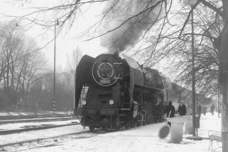  Parný rušeň 475.101 + súprava Ba počas pobytu v stannici. Pohľad zľava zpredu. Vpravo nástupište s cestujúcimi, lavička a osvetlenie. Foto: K. Vaculovič, cca 1975. 180 x 130 