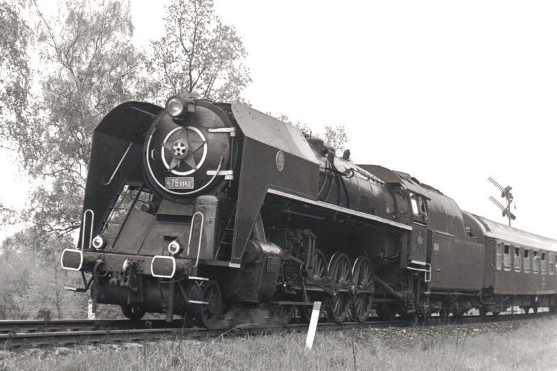  Parný rušeň 475.1142 + Ba. Pohľad zľava zpredu. Za vozňom dvojramenné vchod. návestidlo. Anon., cca 1975. 180 x 128 