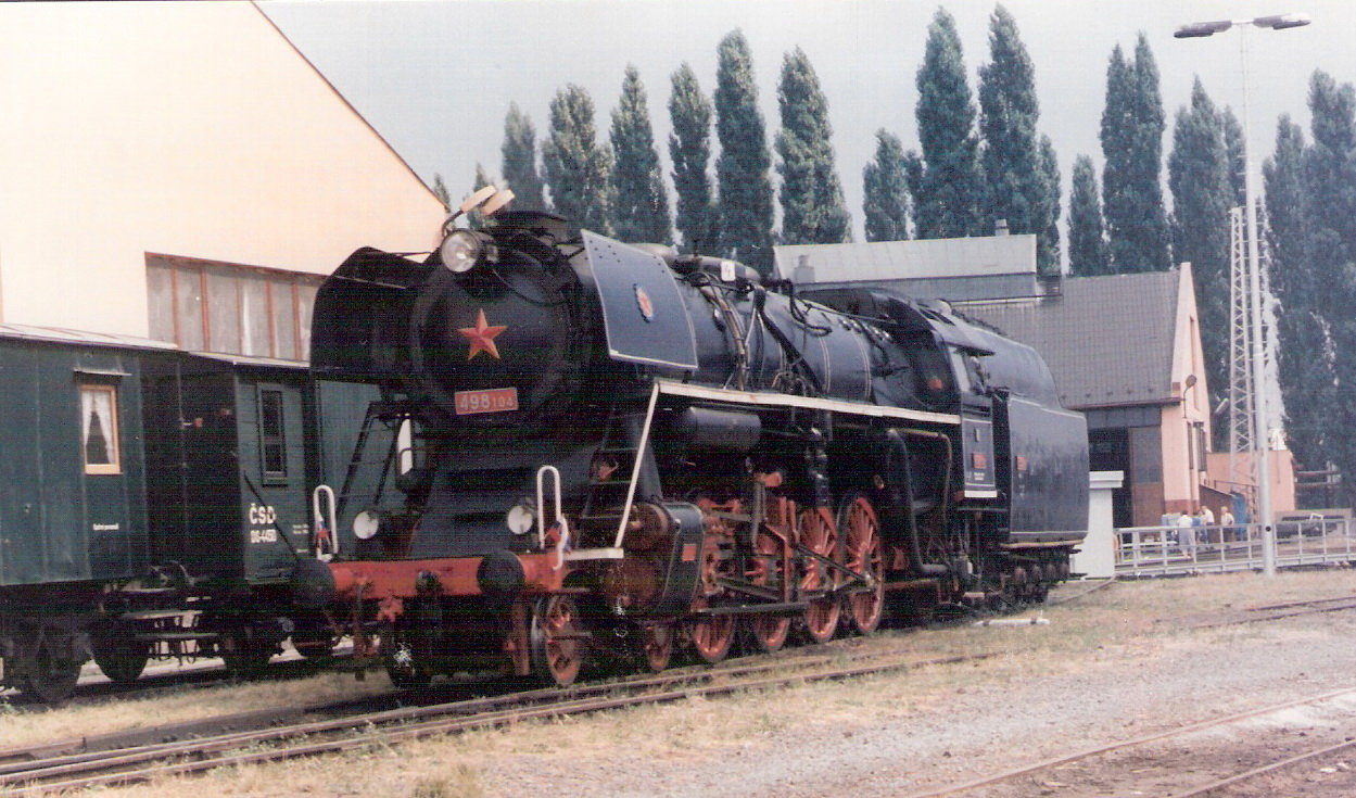  Parný rušeň 498.104 v RD Olomouc. Pohľad zľava zpredu. Vzadu rotunda, točňa a kraj kabíny 310.001. Foto: M. Entner, cca 2000. 173 x 126, COLOR 