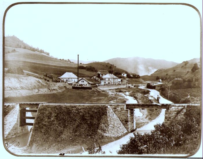  Priemyselný závod, do ktorého zľava ústi žel. vlečka. V popredí žel. trať s drevenými mostami ponad cestu a potok. Hory. Spišská Belá. Text. Pohorelá (?) - továreň na olovené rúry. Foto: Kóczány, 1896. 225 x 175 