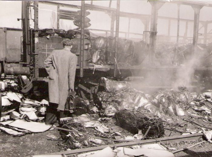  Bratislava sriaď. nádražie. Rozbitý a zhorený krytý nákl. vozeň v smerovej skupine po bombardovaní. Úradník pri obhliadke. Anon., 1945. 123 x 81 