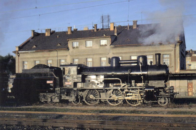  Parný rušeň 354.7152 v žst. Praha Bubny. Pohľad zprava. Vzadu obytná budova. Anon., 14.9.1997. 148 x 105, COLOR. Pohľadnica 