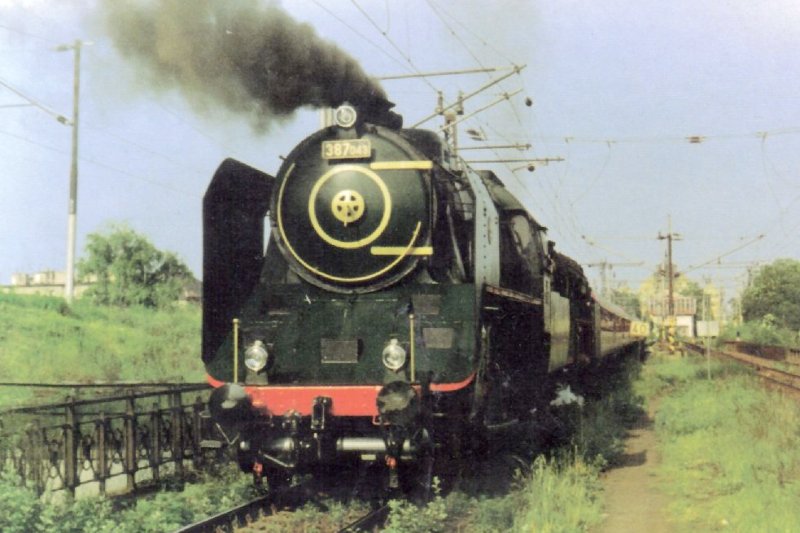  Parný rušeň 387.043, za ním 01 150 DB a podvozk.os. vozne na dvojkoľ. elektrifik. trati. Pohľad zpredu. Vľavo liatinové most. zábr. a ďalšia elektrifik. trať. Vzadu výpr. budova Plzeň hl. n. Foto: M. Venclík, 20.5.1993, 147 x 104. Pohľadnica 