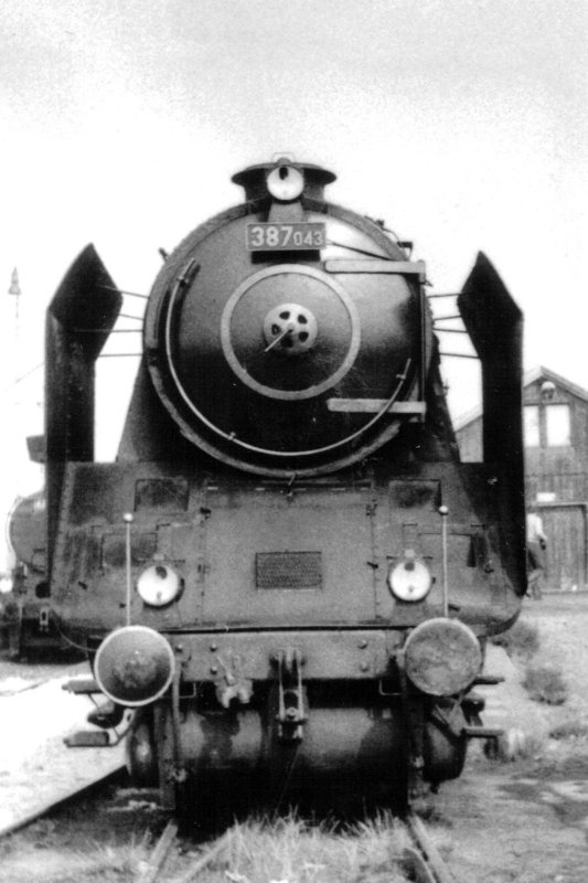  Parný rušeň 387.043 v stanici Nymburk-město. Pohľad zpredu. Vpravo drevený sklad, vľavo okraj 434.1100. Anon., 17.9.1982. 84 x 123 
