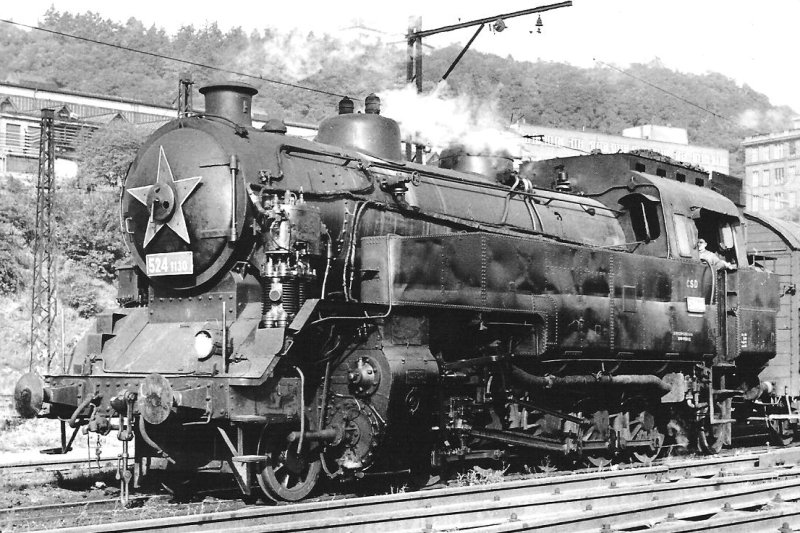  Parný rušeň 524.1130 + Ztr v Prahe (?). Pohľad zľava zpredu. Trolej. Vzadu zalesnený svah s adm. budovami. Foto: P. Vančura, cca 1965. 144 x 102. Pohľadnica Pressfoto Praha 