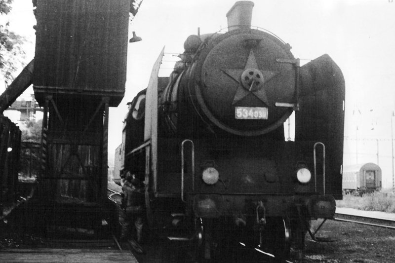  Parný rušeň 534.0311 v depe Bratislava hl. pri hranici depa. Pohľad zpredu. Vľavo odpopoľ. veža, vzadu portálový žeriav, vpravo okraj vodného žeriavu. Foto: J. Kubáček, leto 1975. 240 x 147 