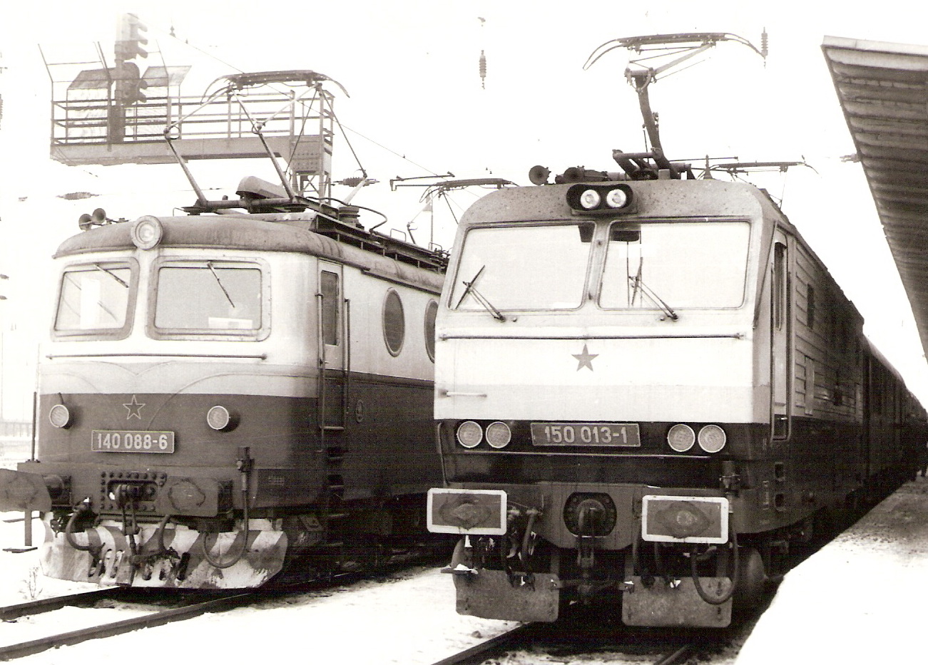  Elektrické rušne 140 088-6 a 150 013-1 vedľa seba v žst. Žilina. Zimný pohľad predobočný. Vľavo vzadu návestidlo ZSSR na krakorci, vpravo kryté nástupište. Foto: O. Čížek, cca 1988, 166 x 120 