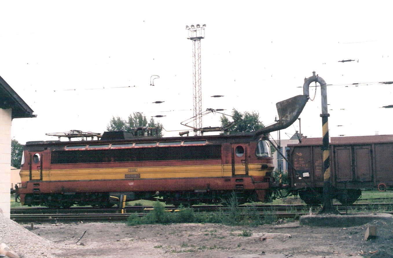  Elektrický rušeň 240 046-3 s nákladným vlakom vchádza do žst. Bratislava východ od Rače. Pohľad zboku. Vpravo vpredu vodný žeriav, vľavo trpaslík AŽD a roh malej vodárne. Vzadu osvetľ. maják. Foto: M. Entner, 8.1998. 178 x 126, COLOR 
