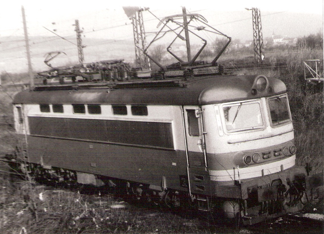  Elektrický rušeň 242.072 - 3 v Kutnej Hore. Pohľad predobočný. Vzadu elektrifik. trať, za ňou obec s kostolom. Foto: Anon., 28.2.1990, 145 x 105. 