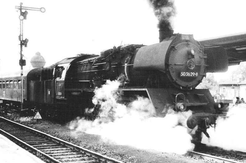  Parný rušeň 50 3629-8 v žst Halberstadt pri krytom peróne. Pohľad zprava zpredu. Vľavo mechanické návestidlo DR, vzadu guľový vodojem vodárne. Foto: Anon., 14.8.1983. 122 x 84 