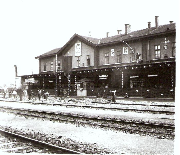  Nitra - výpravná budova. Šikmý pohľad zo strany koľají na leopoldovskú časť priečelia. Socialistická výzdoba. Foto: Anon., cca 1950. 97 x 83 