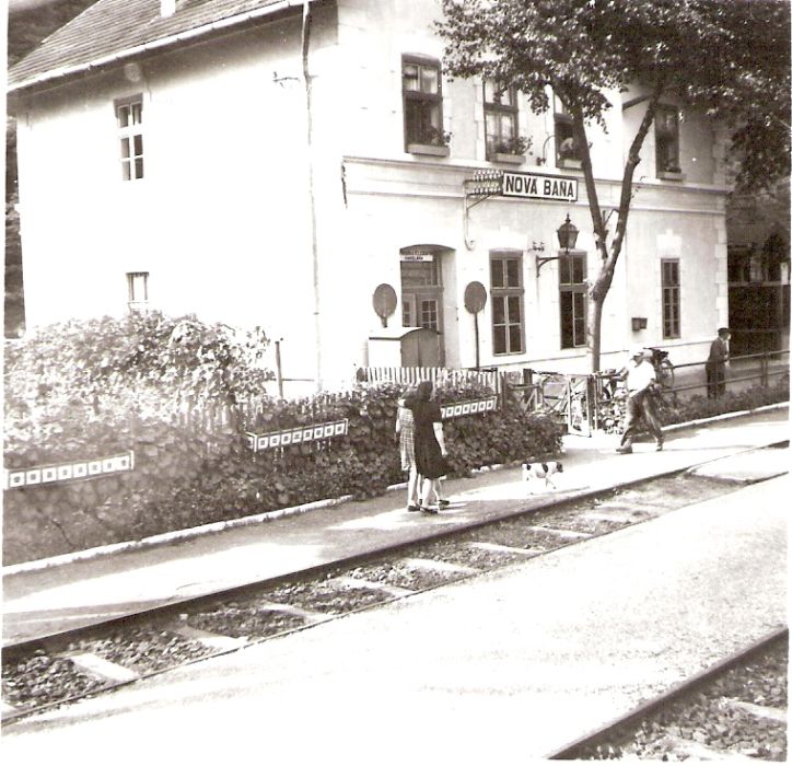  Nová Baňa - výpravná budova. Šikmý pohľad zo strany koľají od Levíc. Konzola s petrolejovou lampou. Ľudia. Foto: Anon., cca 1950. 95 x 93 