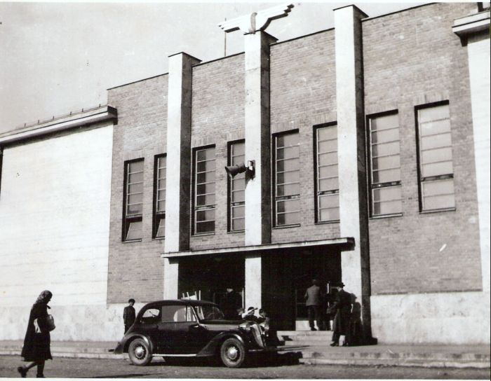  Považská Bystrica - výpravná budova nová. Čelný pohľad na predstaničné priečelie. Pred budovou osobný automobil. Amplión. Foto: Anon., cca 1950. 166 x 120 