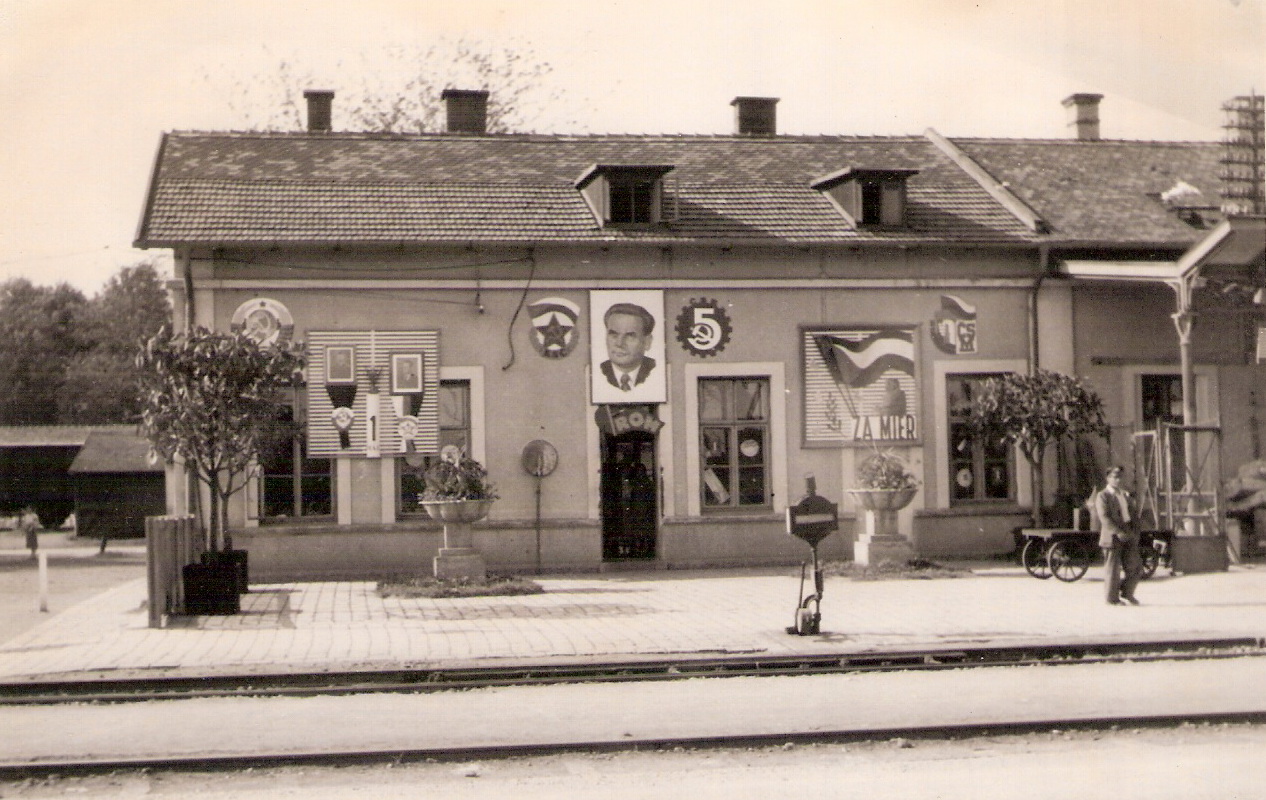  Trnava - výpravná budova stará. Čelný pohľad zo strany koľají na bratislavské krídlo. Výhybka s kruhovou lampou. Prvomájová výzdoba. Foto: Anon., cca 1950. 162 x 110 