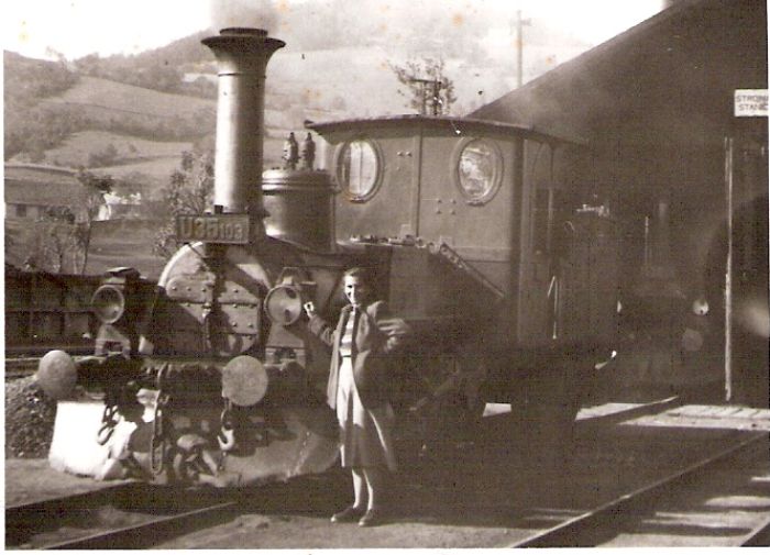  Úzkorozch. parný rušeň U 35.103 pred remízou v Banskej Štiavnici. Pohľad zľava zpredu. V remíze ďalší rušeň U 35.1. Pri rušni stojaca žena. Vzadu kopce. Foto: Ing. Héger, 1949. 84 x 60 