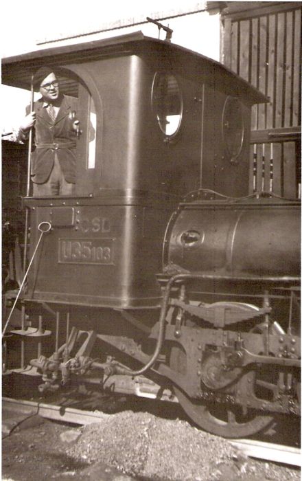  Úzkorozch. parný rušeň U 35.103, zrejme v Banskej Štiavnici. Pohľad na kabínu rušňa a 3. nápravu zprava. Na stanovišti rušňovodiča muž v civile. Vzadu múr budovy, o kabínu opreté ohreblo. Foto: Anon., 1949. 80 x 129 