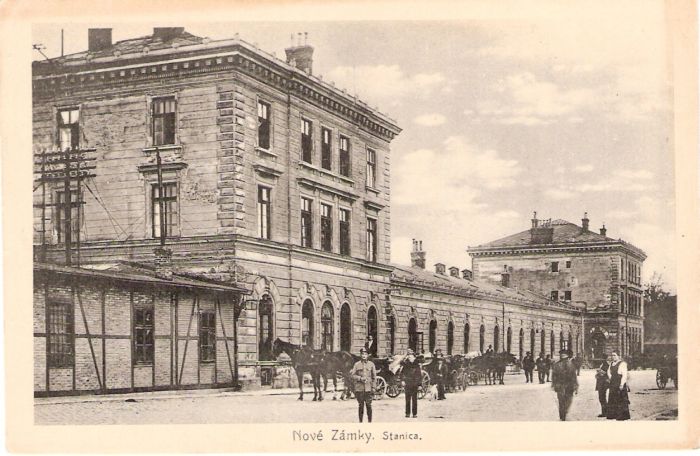  Nové Zámky - výpravná budova. Šikmý pohľad z predstaničného priestoru od Bratislavy. Kone, koče, ľudia v civile i rovnošatách. Foto: Anon., cca 1920. 129 x 80 