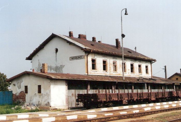  Michalovce - výpravná budova. Šikmý pohľad zo strany koľají od Košíc. Osvetľovacie stožiare, pred budovou štvornápravový nízkostenný vozeň. Foto: K. Kočiško, cca 2000. 125 x 88, COLOR 