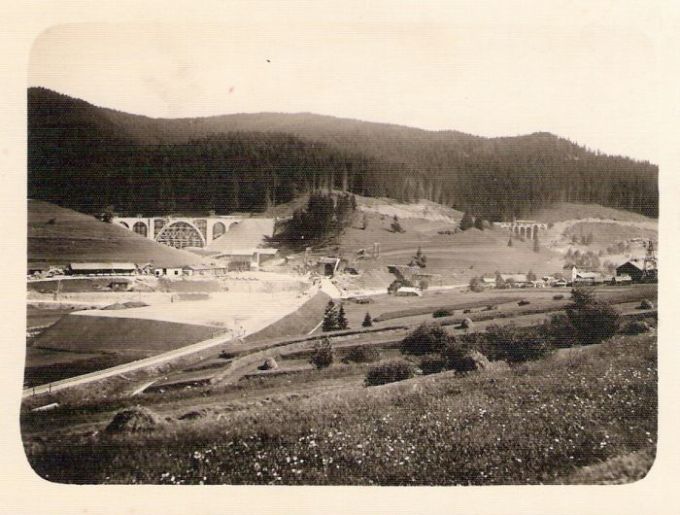  Stavenisko pri zastávke Telgárt-penzión počas výstavby trate. Panoramatický pohľad od Telgártu. Vľavo i vpravo rozostavané viadukty, dole ústie špirál. tunela a rozostavaná trať, lanovka, budovy staveniska, hory. Foto: Anon., cca 1933. 105 x 75 
