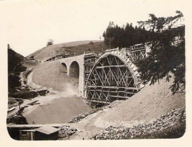  Viadukt nad zastávkou Telgárt-penzión počas stavby. Šikmý pohľad sponad spodného portálu telgártskeho tunela. Drevené lešenie skruže hlavného oblúka mosta. Foto: Anon., cca 1932. 104 x 70 