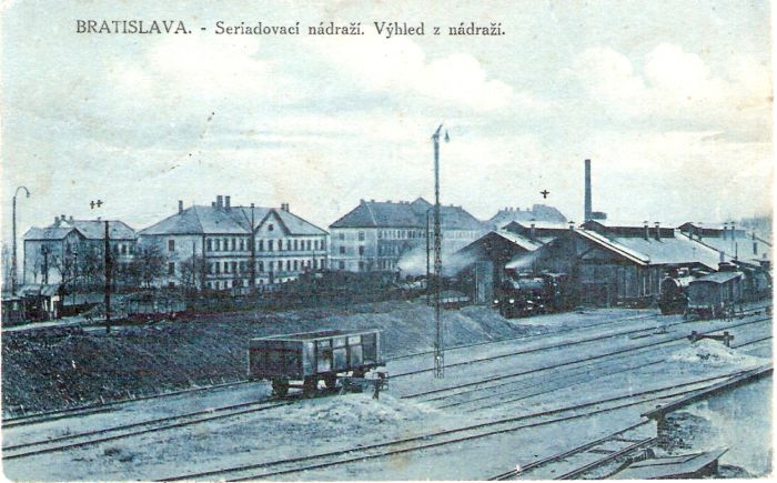  Bratislava východ - staré rušňové depo. Pohľad od pers. kuchyne k remíze a železn. kolónii. Remíza, rušne, vyviazaný vozeň, komín elektrárne, obytné budovy. Foto: Anon., cca 1918. 138 x 88 