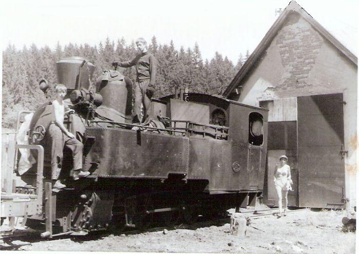  Úzkorozch. parný rušeň Henschel Zákamenskej lesnej železnice pred remízou v Tanečníku. Pohľad zľava zpredu. Na rušni zľava Z. a J. Kubáček, vpravo L. Kubáčková. Foto: L. Kubáček, cca 1974. 98 x 67 