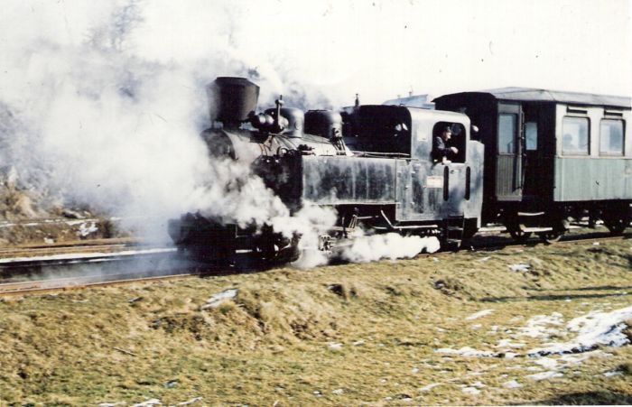  Úzkorozch. parný rušeň C 760/90d Vígľašskej lesnej železnice tlačí tramvajový dvojnápravový príves v neidentifik. stanici. Pohľad zľava zpredu. Foto: Anon., cca 1970. 152 x 100, COLOR 