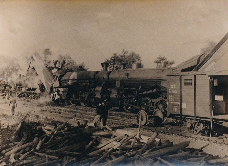Nehoda v Hričove 28.9.1941. Čelne zrazené rušne 375.0 vľavo a 455.1 vpravo, za rušňom 375.0 dohárajúce trosky cisternových vozňov s naftou, vpravo krytý vozeň SŽ, v popredí rozsypaná guľatina, za ňou kráčajúci ľudia. Text: Nehoda v Hričove - v roku 1941. Foto: Ján Štukovský, 28.9.1941.