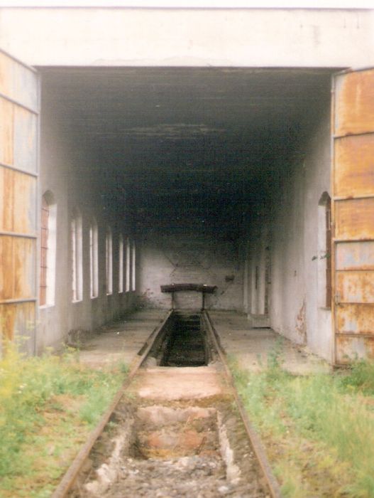  Rajec - depo. Čeloný pohľad v osi koľaje na koľaj s kanálom v interiéri cez otvorenú bránu depa. Foto: M. Entner, 17.8.1996. 89 x 126, COLOR 