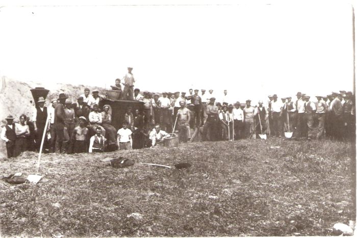  Parný rušeň úzkorozch. Orenstein a Koppel s drevenými huntíkmi. Pohľad zľava. Množstvo ľudí v pracovnom i v civile, niektorí s lopatami a s košmi. Foto: Anon., cca 1930, zb. P. Faturu, Ladce, fotokópia. 143 x 92 