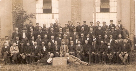  Skupina mužov (civil, prac. obleč. i rovnošaty) pred dielen. budovou s tabuľou: Dielňa ČSD Zvolen, odd.II., 21.7.1924. Anonym, 135 x 85 mm. 
