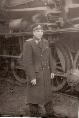  Postava muža v železničnej rovnošate pred parným rušňom. Bez textu. Anonym, cca 1960. 120 x 80 