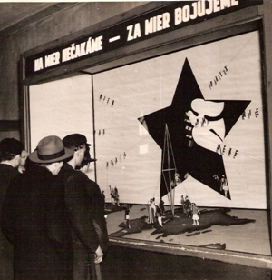  Skupina ľudí v civile pred výkladom s mierovou agitáciou (hviezdou a holubicou). Text: Žst. Bratislava hl. Anonym, cca 1950. 127 x 123 