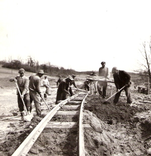  Skupina robotníkov s lopatami na prac. drážke. Text: Pracovné brigády pracujú na novej trati 1. mája Selce - Nograd Szakal. Foto: Kľučka, cca 1955. 127 x 123 