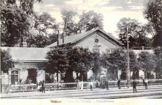  Senec - výpravná budova. Čelný pohľad zo strany koľají. Konzolový mrežový stožiar elektrického osvetlenia. Ľudia. Foto: Anon., cca 1930, farebná xerokópia. 262 x 162 