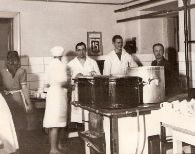  Skupina ľudí v bielych plášťoch a v civile v prostredí závodnej kuchyne. text: Železničná kuchyňa. Anonym, cca 1950. 138 x 108 